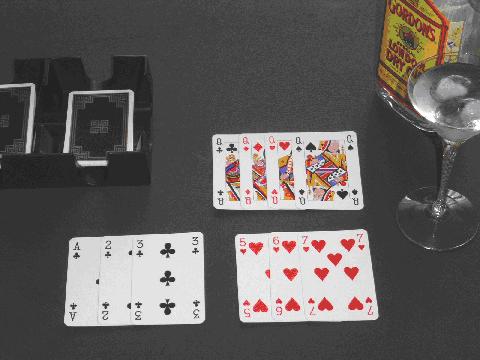 A completed game of Rummy Gin Card Game showing 3 melds with no deadwood, as well as a glass and bottle of Gin to the right